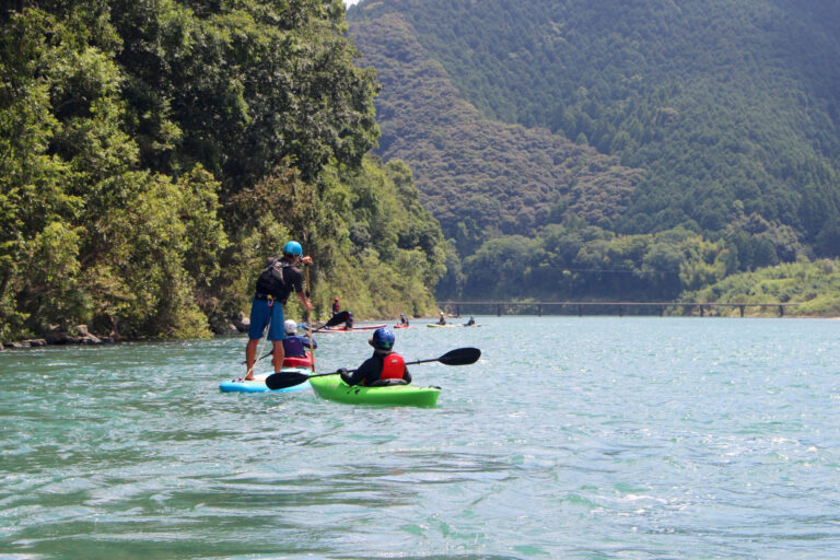 四万十川でカヤックとSUPを楽しむ体験者たち。緑豊かな山と清流を背景にしたアウトドア体験の様子