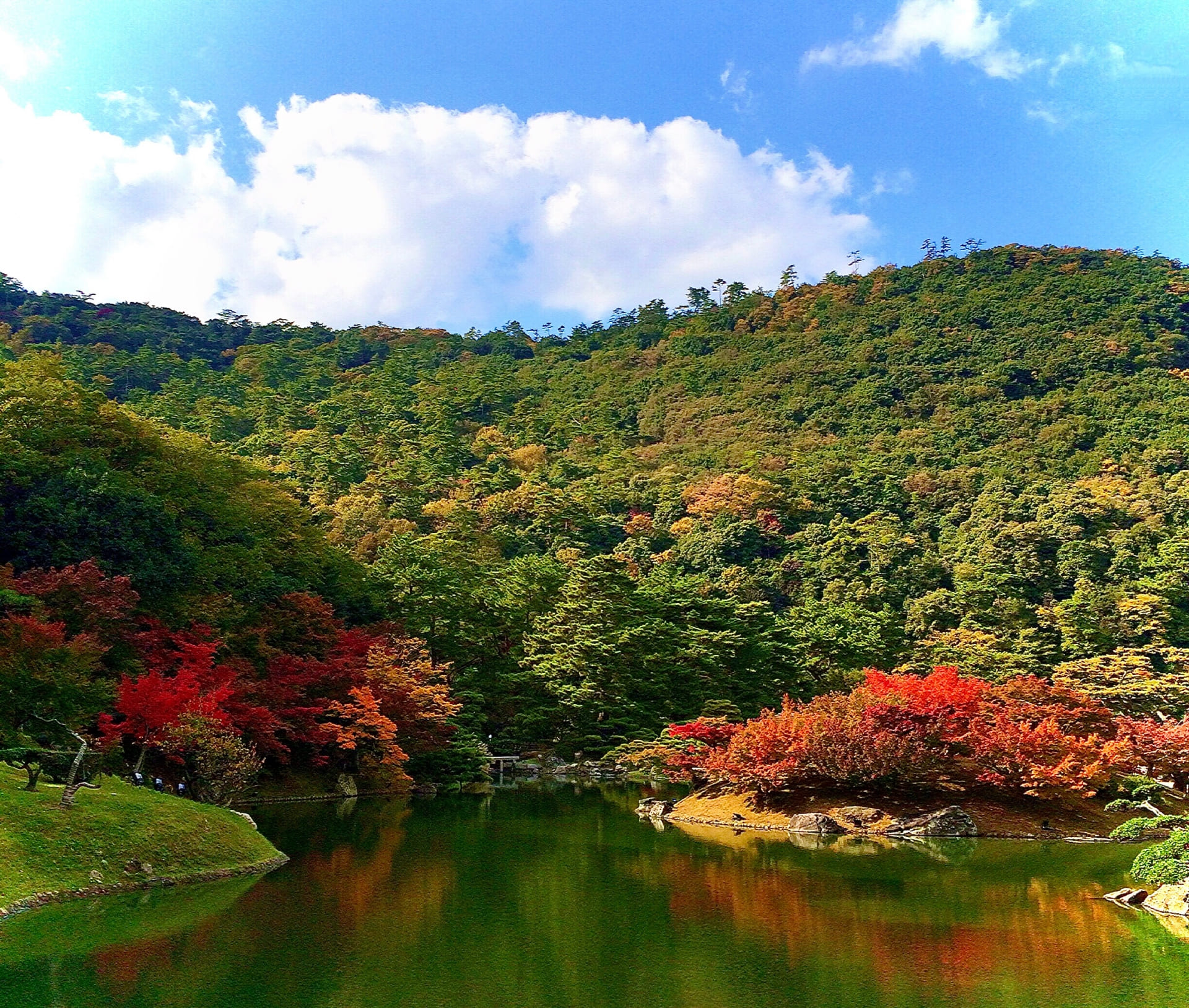 栗林公園の秋の紅葉。赤や黄に染まった山の木々が池の水面に映り込む