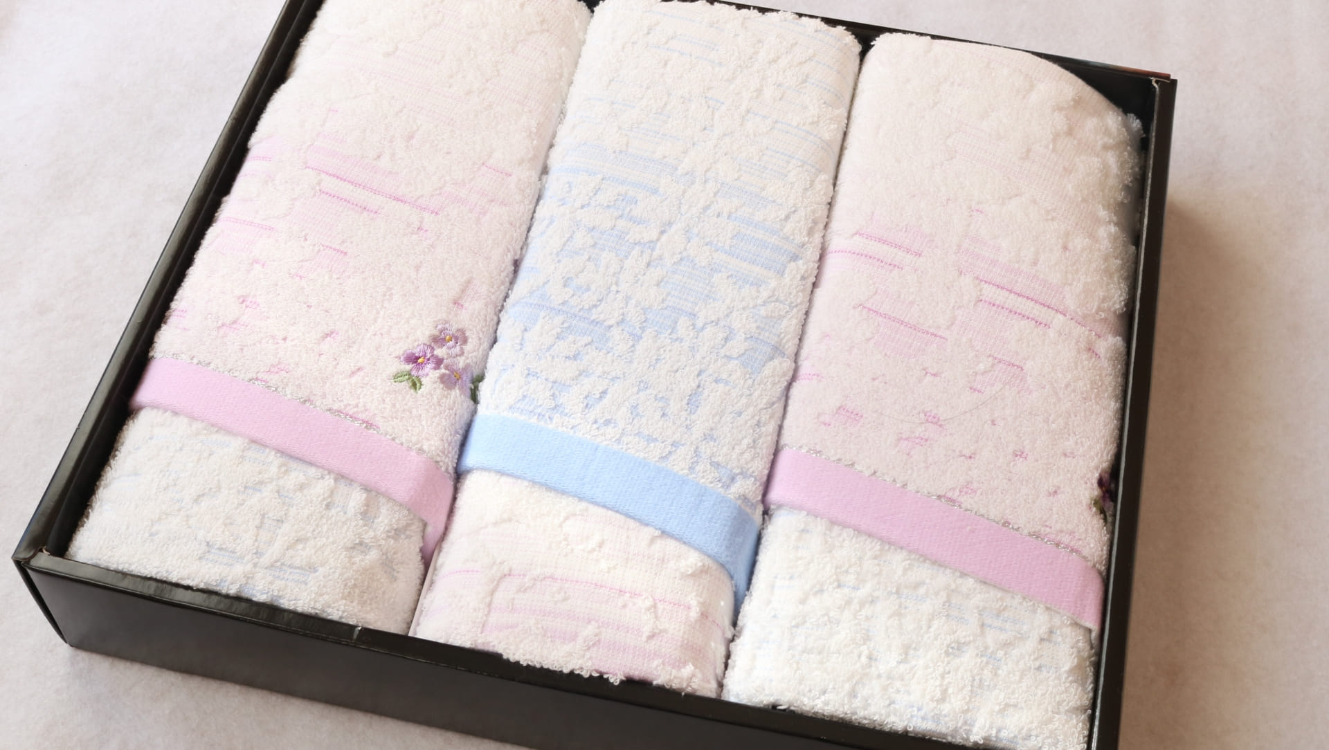 箱に丁寧に収められた今治タオルのギフトセット。ピンクと水色のリボンがかかった白いタオルが3枚並ぶ