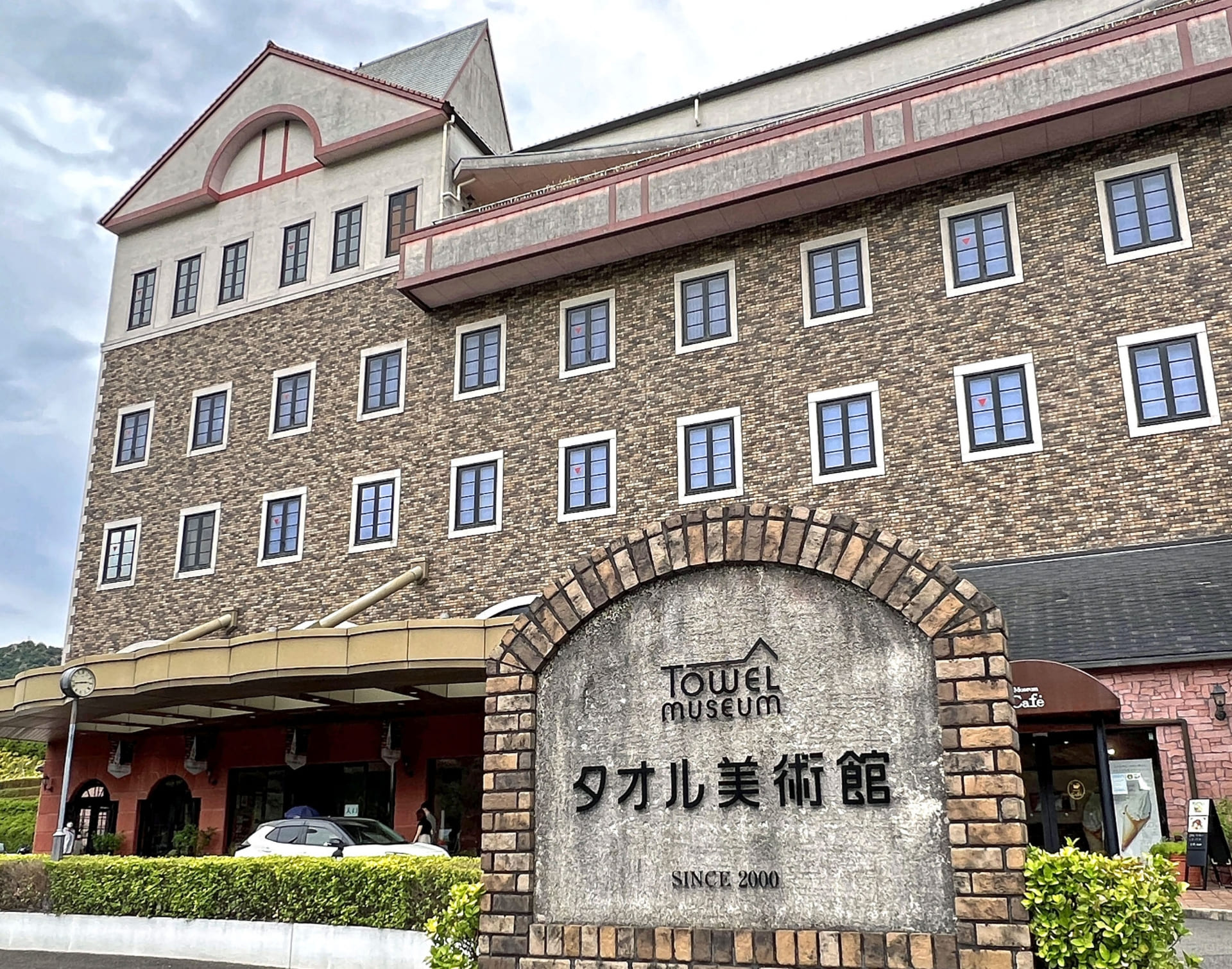 タオル美術館（ichihiro）の外観。レンガ調の建物に「Towel museum タオル美術館 SINCE 2000」の石碑が立つ