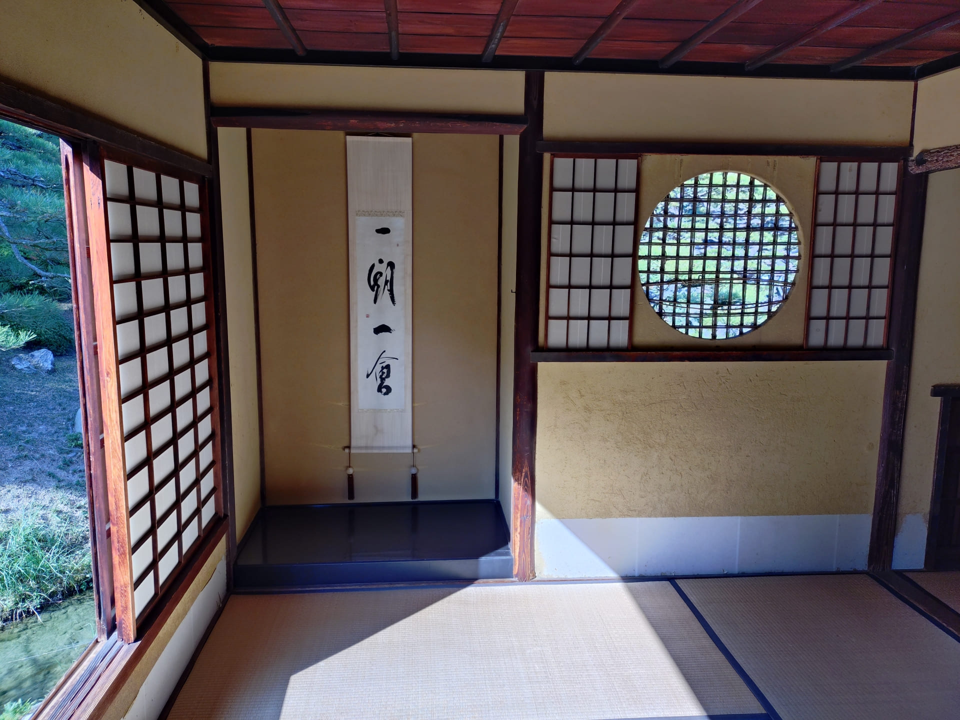 栗林公園の茶室内部。丸窓から庭の緑が見え、床の間に「一期一会」の掛け軸が飾られた畳の間