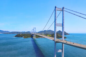 来島海峡大橋の全景。青空と瀬戸内海を背景に3連の吊り橋がのびる（愛媛県今治市）