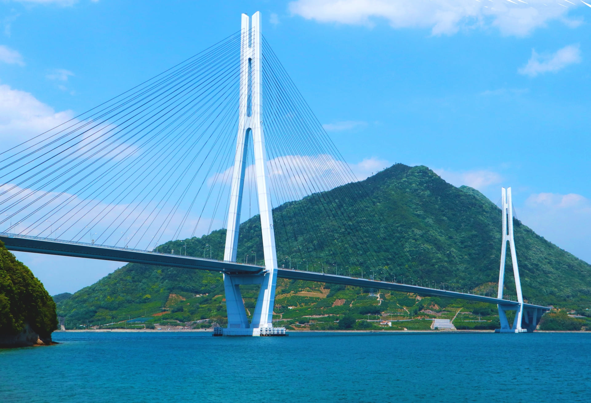 多々羅大橋の全景。斜張橋が青い瀬戸内海と緑の山を背景に弧を描く