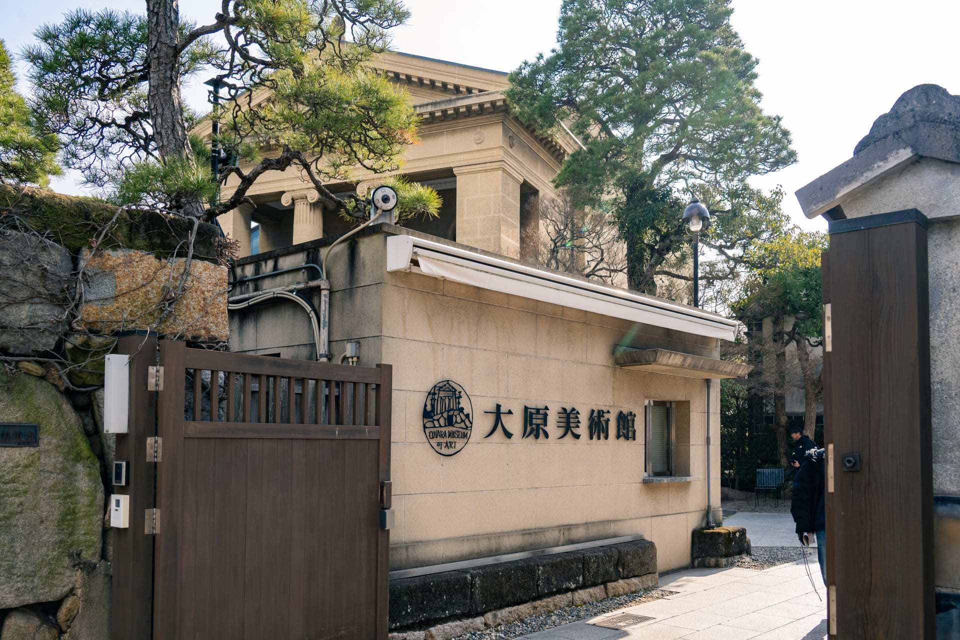 大原美術館の入口。石造りの門扉に「大原美術館」の看板が掲げられ、背後に重厚な石造りの建物が見える